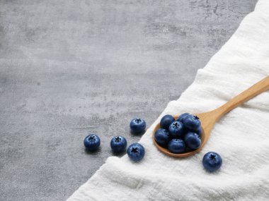 Ahşap kaşıkta yaban mersini ve taş kaplama arka planda kumaş.