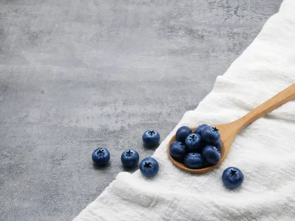 Ahşap kaşıkta yaban mersini ve taş kaplama arka planda kumaş.