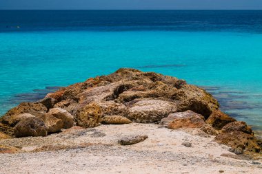 Arkasında kayalar ve turkuaz deniz olan güzel bir sahil.