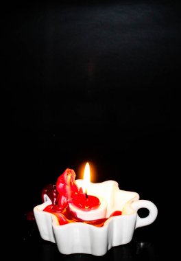 Erimiş mum damlayan, beyaz bir dekoratif tutacağında yanan bir mum. Arka plan siyahtır, dramatik bir kontrast yaratır. Alev hafifçe yanıp sönüyor, balmumunu aydınlatıyor..