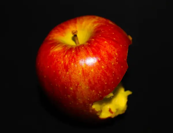 stock image A close-up of a partially eaten red apple with a yellow interior, set against a black background.