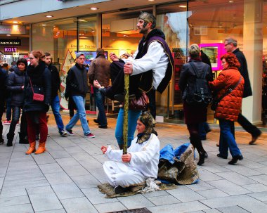 Beyaz cüppeli sokak sanatçıları, biri yerde oturuyor ve diğeri direğin üzerinde yükseliyor, kalabalık bir alışveriş merkezinde kalabalığı eğlendiriyorlar..