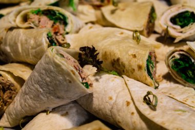 Yeşillik ve et gibi çeşitli malzemelerle dolu rulo tortillaların yakın çekim görüntüsü, düzgünce bir tabakta dizilmiş..