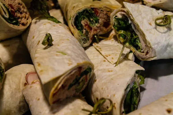 stock image A close-up view of rolled wraps filled with greens, meats, and spreads, arranged on a surface. The wraps are neatly rolled and garnished with green herbs.