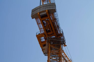 Bir inşaat vincinin açık mavi gökyüzüne yakın görüntüsü, yapısını ve makinelerini gösteriyor..