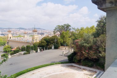 Şatafatlı bir şehir manzarası, yemyeşil, süslü bir mimari ve dolambaçlı bir yol. Arka plan bulutlu bir gökyüzünün altında, uzak dağların olduğu bir ufuk çizgisi gösteriyor..