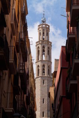 Uzun, tarihi bir çan kulesi şehrin dar binaları arasında yükseliyor. Mavi gökyüzüne karşı karmaşık mimari detaylar sergiliyor..