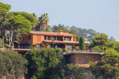 Güzel bir Akdeniz tarzı villa, yemyeşil ve palmiye ağaçlarıyla çevrili bir uçuruma tünemişti. Ev, manzaranın çarpıcı manzarasını sunan bir terracotta çatısı ve geniş pencerelere sahip..
