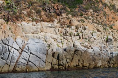 Geniş, dokulu kayaları ve dik bir uçurumu olan kayalık bir sahil şeridi. Su sakindir ve kayalık oluşumları yansıtır. Uçurumun çevresi yeşilliklerle çevrilidir..