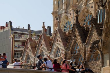 Visitors admiring the intricate architecture of a famous building with unique stonework and decorative elements. The scene captures a sunny day with people engaged in photography. clipart