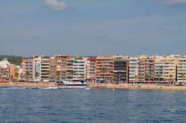 Renkli binalar ve palmiye ağaçlarıyla kaplı bir sahile sahip bir sahil manzarası. Denizde bir tekne görüldü, insanlar sahilde eğleniyorlardı..