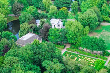 Manikürlü bahçeler, bir gölet ve sık ağaçlarla çevrili birkaç binanın bulunduğu yemyeşil bir parkın havadan görünüşü. Manzara doğa ve mimarinin uyumlu bir karışımını sergiliyor..