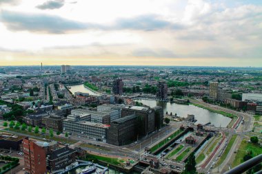 Nehirlerin, modern binaların ve bulutlu bir gökyüzünün altında yeşil alanların bulunduğu panoramik bir manzara. Sahne, şehir planlarını yollar ve su yollarıyla yakalıyor..