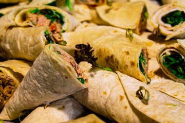 Yeşillik ve et gibi çeşitli malzemelerle dolu rulo tortillaların yakın çekim görüntüsü, düzgünce bir tabakta dizilmiş..