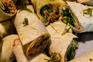 Yeşilliklerle, etlerle ve yayıklarla dolu, bir yüzeye dizilmiş dürülmüş paketlerin yakın çekim görüntüsü. Sargılar düzgünce sarılmış ve yeşil otlarla süslenmiş..