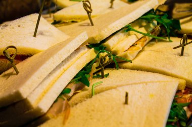 Beyaz ekmekli, yeşil otlarla süslenmiş ve kürdanla sabitlenmiş düzgünce hazırlanmış sandviçler. Sandviçler taze ve servis için hazır görünüyor. Dolgu tabakaları sergileniyor..