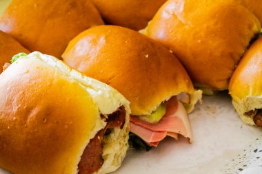 Yumuşak, altın sarısı çöreklerle yeni yapılmış birkaç sandviçin yakın plan görüntüsü. Bazı sandviçler meze, marul ve turşu katmanları ile doludur. Lezzetli malzemeler sergilenir..