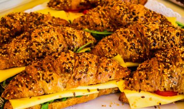 Peynir, marul ve domatesle dolu, düzgünce bir tabakta dizilmiş susam tohumlu kruvasanların yakın plan görüntüsü..