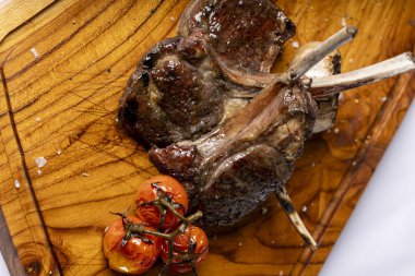 Izgara kuzu pirzolası, kavrulmuş kiraz domatesleri ve sarımsak, ahşap bir tahtada kaba deniz tuzu ile servis edilir..