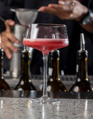 Bir barmen bardağa kokteyl dökerken ince bir ağ süzgeci kullanır. Bar ortamında profesyonel miksoloji teknikleri sergiler..