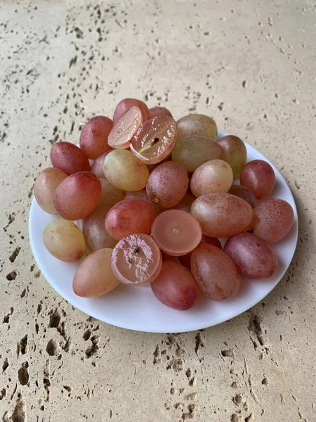 Individual berries of pink grapes on a white plate close-up. Still life on a concrete background. Two berries cut in half.