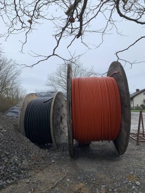 İnşaat alanında iki makaralı elektrik kablosu yan yana duruyor. Birinde turuncu kablo, diğerinde siyah kablo var. Dikey fotoğraf.