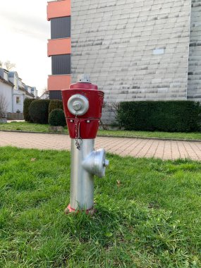 Bir Alman köyünün yakınındaki yeşil çimlerin üzerinde kırmızı gümüş bir yangın musluğu duruyor. Yakın plan. Dikey fotoğraf.