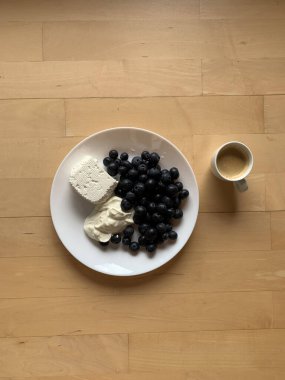 Bir fincan espresso kahve ve ahşap zemin üzerinde süzme peynir, ekşi krema ve yabanmersini standı olan bir tabak. Yukarıdan bak. Mesaj için yer. Kahvaltı..