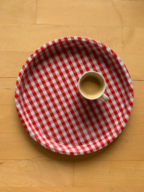 Beyaz ve kırmızı gingham kaplı yuvarlak bir tepsi ve bir fincan espresso kahvesi ahşap arka planda duruyor. Yukarıdan görüntüle.