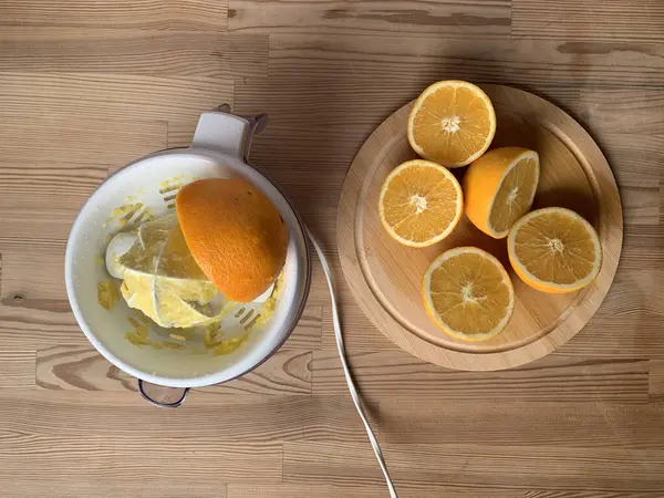 Portakal suyu hamurlu Citrus elektrik sıkacağı. Yakınlarda, ahşap bir masanın üzerinde yuvarlak ahşap bir tahta üzerinde beş turuncu yarım bulunuyor. Evde portakal suyu sıkma süreci devam ediyor. Yukarıdan görüntüle.