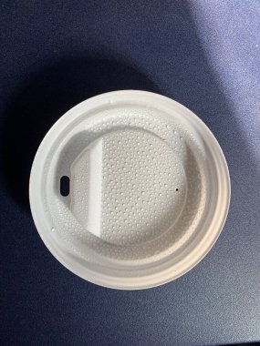 Mavi plastik bir masanın üzerinde tek kullanımlık beyaz bir kahve fincanı kapağının yakın çekimi. Kapağın içi sıcak içecekten gelen küçük buhar damlacıklarıyla dolu. Hazır kahve, rahatlık ve modern yaşam tarzıyla ilgili kavramlar için mükemmel..