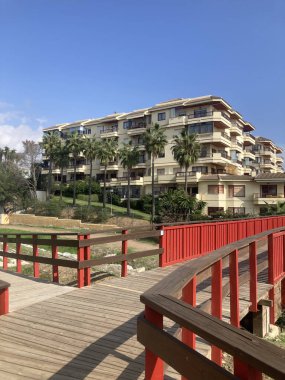 Palmiye ağaçları ve Endülüs, İspanya 'da kırmızı parmaklıkları olan tahta yaya köprüsü olan modern bir yerleşim yeri. Akdeniz 'de manzaralı kentsel mimari.