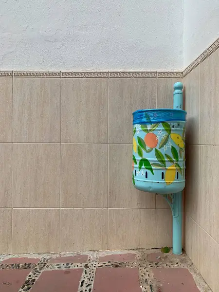 Marbella, Endülüs, İspanya 'da kiremit kaplı bir duvarda narenciye desenli elle boyanmış çöp kutusu. Mavi ve sarı sanat eserleri şehir düzenine cazibe katıyor.
