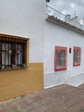 Marbella, İspanya 'da geleneksel bir evin renkli yüzü. Beyaz duvarlar, sarı ve pembe pencere çerçeveleri, demir parmaklıklar ve kil kil kaldırım büyüleyici bir görünüm yaratır..