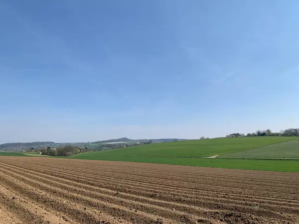 Ön planda yeni sürülmüş tarlaları ve açık mavi gökyüzünün altında yemyeşil tepeleri olan manzaralı kırsal bölge. Orta Avrupa 'da tipik bir bahar mevsimi için huzurlu bir kırsal manzara.