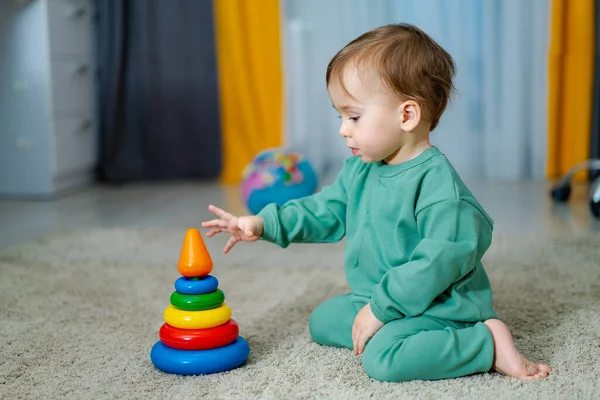 Baby playing with pyramid toy. Cute little boy is playing with toys while sitting on floor.Happy toddler baby boy sorting colorful rings on pyramid