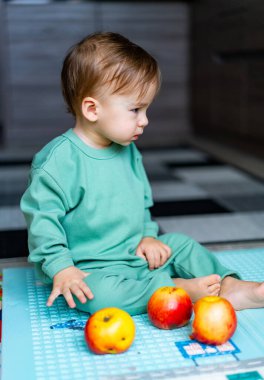 Küçük oğlan mutfakta oturmuş meyve elması yiyor. Evde elma yiyen tatlı bir erkek bebek. Sağlıklı çocuk beslenmesi