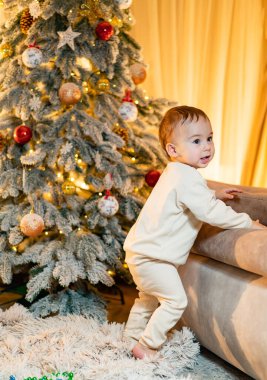 Noel, tatil ve çocukluk konsepti. Noel ağacının yanında şirin bir çocuk. Ev için büyülü şenlik dekorasyonu