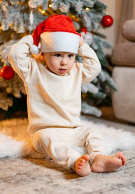 Noel zamanı. Noel ağacının yanında şirin bir çocuk. Noel Baba şapkalı küçük bir çocuğun portresi. Yeni Yıl