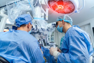 Mikroskoplu doktorlar. Mavi üniformalı sağlık çalışanları mikroskoptan bakarken hastaya operasyon yapıyorlar..  