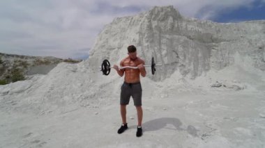 Adam dağda eğitim görüyor. Sporcunun antrenman kıyafetleri içinde, halterle dağın tepesinde dikilirken.