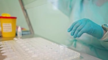 Kan testi için hazırlık. Doktor el, laboratuvar arka planında analiz makineleri olan bir raftan kan örneği alıyor.