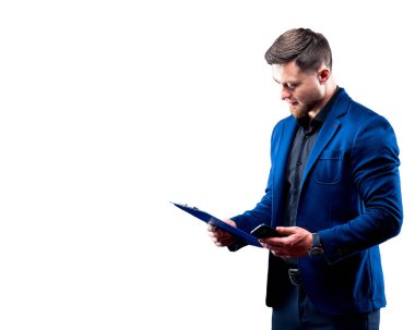 Portrait of handsome young successful man wearing dark shirt and blue suit holding blue folder, looking at notes. White background. Business concept.