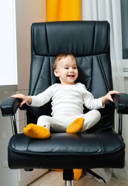 Young attractive kid on leather office chair. Little cheerful baby boss sitting on a chair.