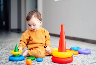 Renkli piramitlerle oynayan küçük bir çocuk. Küçük çocuk oyuncakla oturuyor.