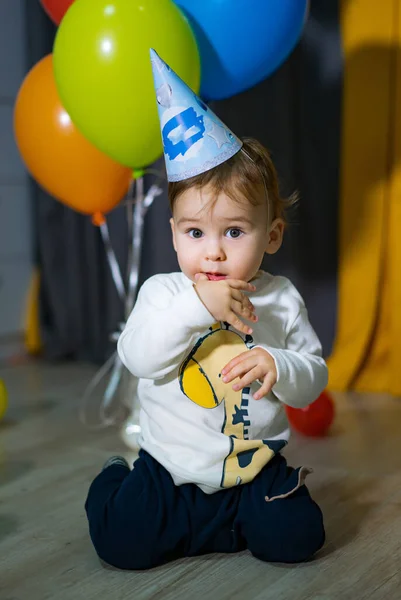 Funny cute baby celebration. Birthday young child with hat and balloons.