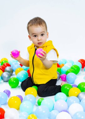 Genç çocuk renkli balonlarla eğlenceli bir anın tadını çıkarıyor. Balonlarla çevrili yerde oturan küçük bir çocuk.