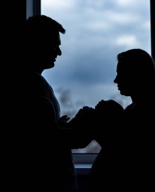 Genç bir ailenin gölgesi ve yeni doğmuş bir bebek. Mutlu ebeveynlerin siluetleri.