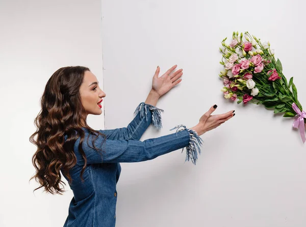 A woman in a denim shirt reaching out towards a bouquet of flowers. Reaching for Blooming Beauty