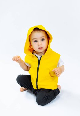 Küçük çocuk şık sarı ceketli açık havanın tadını çıkarıyor. Sarı ceketli küçük bir çocuk yerde oturuyor.